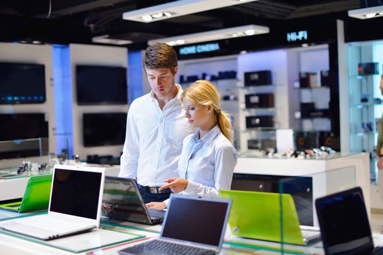Two people looking at laptops in a store.